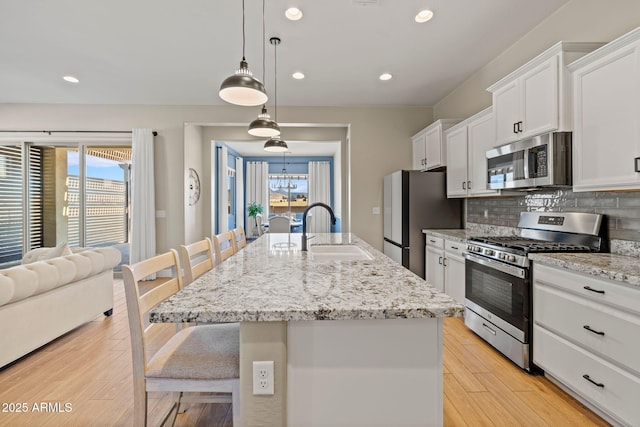 kitchen featuring sink, a breakfast bar, appliances with stainless steel finishes, a center island with sink, and decorative light fixtures