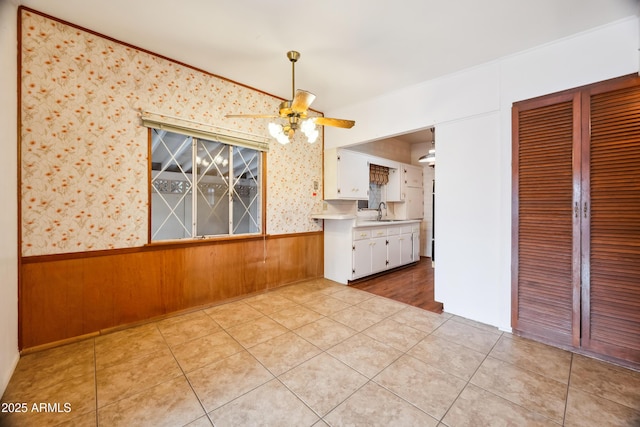 kitchen featuring wooden walls, light tile patterned floors, white cabinetry, ceiling fan, and sink