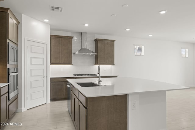 kitchen featuring backsplash, stainless steel appliances, sink, wall chimney range hood, and a center island with sink