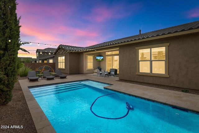 pool at dusk with a patio, fence, and a fenced in pool