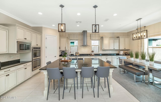 kitchen featuring cream cabinetry, stainless steel appliances, ornamental molding, light tile patterned flooring, and wall chimney range hood