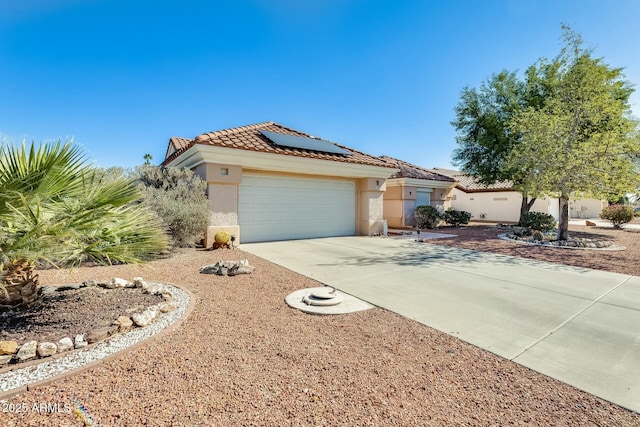 mediterranean / spanish home featuring a garage, a tiled roof, driveway, roof mounted solar panels, and stucco siding