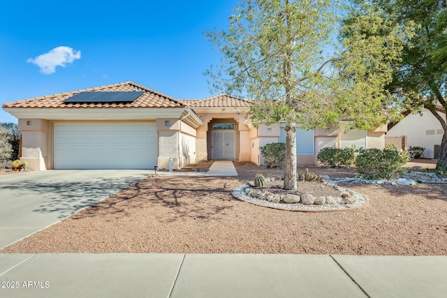 mediterranean / spanish-style house featuring a tile roof, solar panels, stucco siding, concrete driveway, and an attached garage