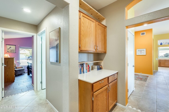 corridor featuring visible vents, baseboards, and light tile patterned flooring