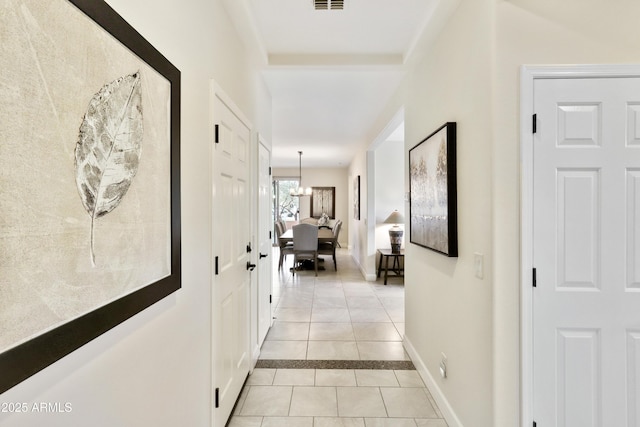 hall featuring light tile patterned floors, visible vents, baseboards, and a chandelier