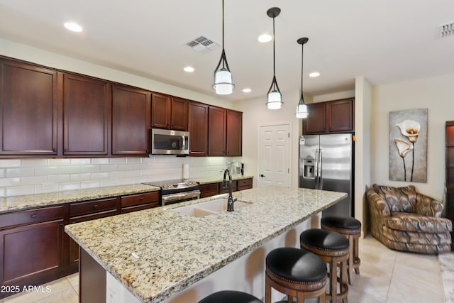 kitchen featuring visible vents, a sink, stainless steel appliances, a breakfast bar area, and decorative backsplash