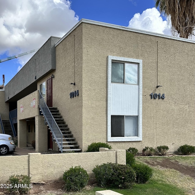 view of side of home with stairs, fence, and stucco siding