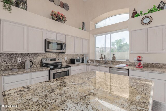 kitchen featuring sink, white cabinets, stainless steel appliances, light stone countertops, and a high ceiling