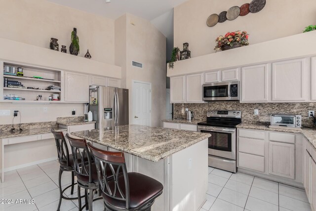 kitchen featuring white cabinets, appliances with stainless steel finishes, light tile patterned floors, and high vaulted ceiling