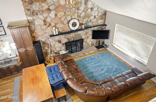 living room featuring vaulted ceiling, a fireplace, a textured ceiling, and light hardwood / wood-style floors