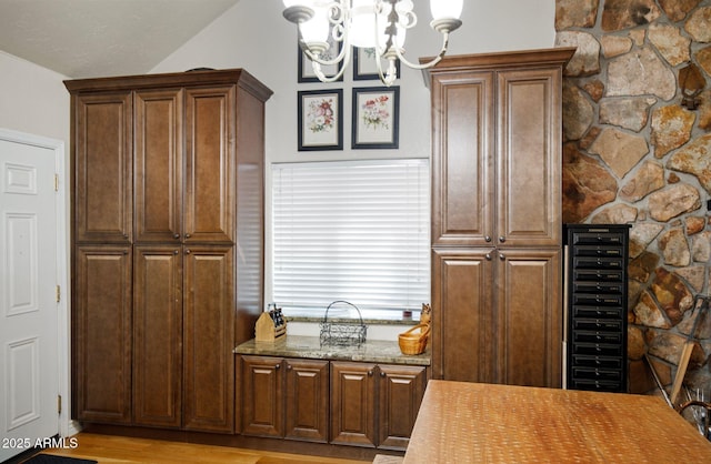 kitchen with vaulted ceiling, a chandelier, wine cooler, light stone counters, and light hardwood / wood-style flooring