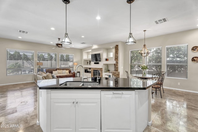 kitchen with a wealth of natural light, dark countertops, visible vents, a sink, and a stone fireplace