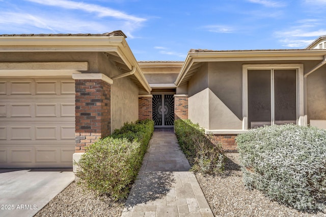 doorway to property featuring a garage, stucco siding, and brick siding