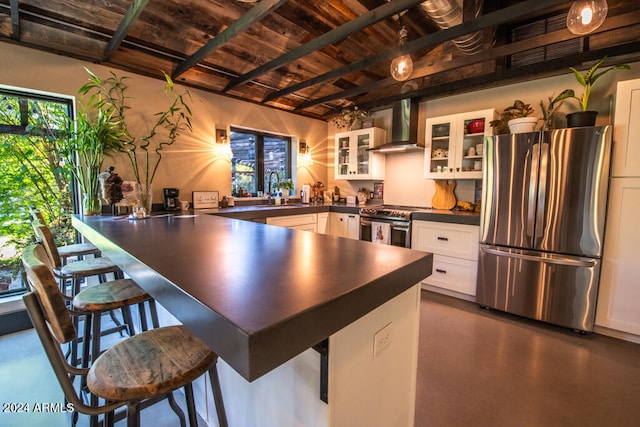 kitchen with wall chimney exhaust hood, a kitchen breakfast bar, sink, white cabinetry, and appliances with stainless steel finishes