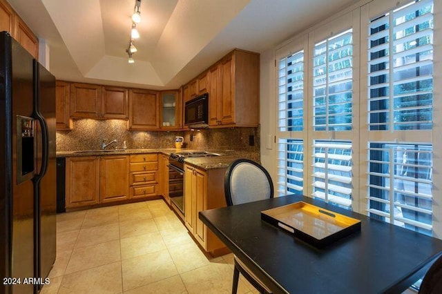 kitchen with black appliances, decorative backsplash, dark stone countertops, light tile patterned flooring, and a tray ceiling