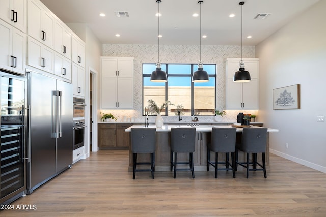 kitchen featuring appliances with stainless steel finishes, white cabinetry, hanging light fixtures, and an island with sink