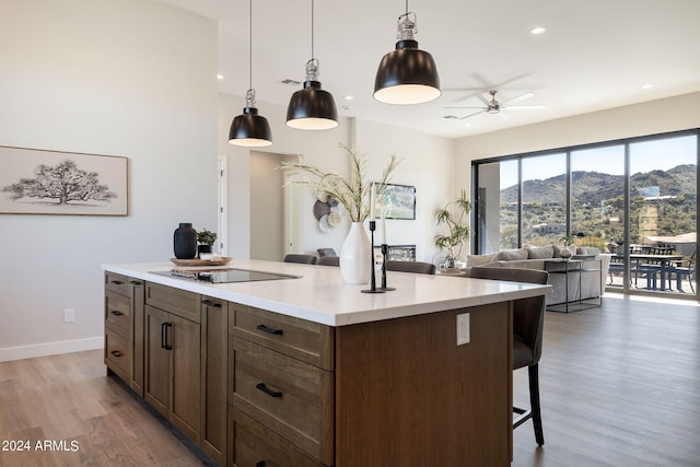 kitchen featuring a mountain view, black electric stovetop, light hardwood / wood-style flooring, ceiling fan, and decorative light fixtures