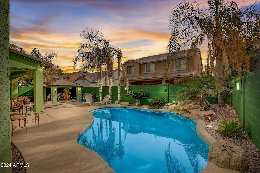 pool at dusk with a patio and a gazebo