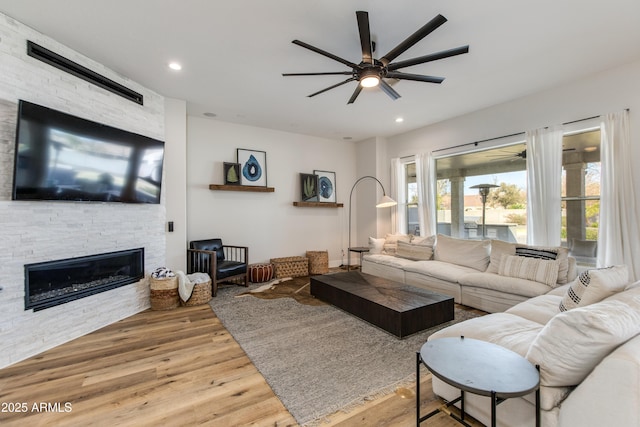 living area with a stone fireplace, wood finished floors, a ceiling fan, and recessed lighting