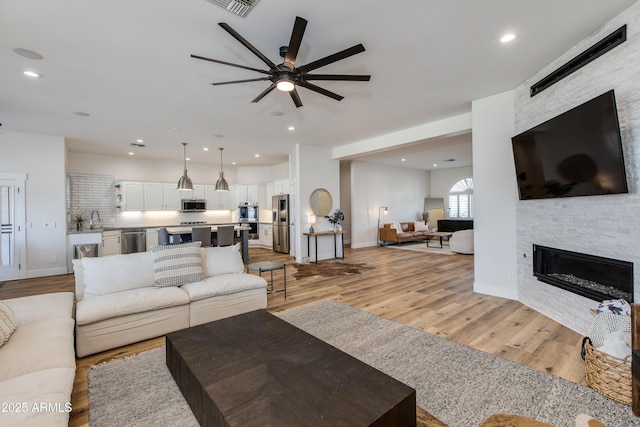 living room featuring baseboards, a stone fireplace, recessed lighting, and light wood-style floors