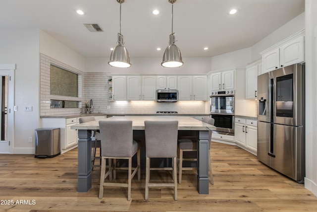 kitchen featuring pendant lighting, visible vents, appliances with stainless steel finishes, white cabinetry, and a kitchen island