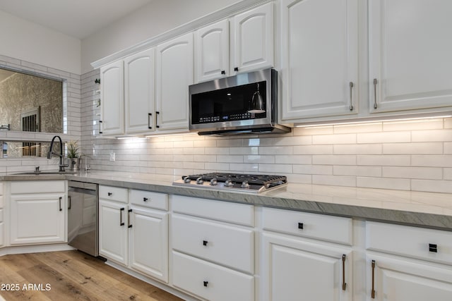 kitchen with a sink, light wood-style floors, white cabinets, appliances with stainless steel finishes, and decorative backsplash