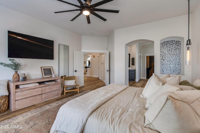 bedroom with arched walkways, wood finished floors, and connected bathroom