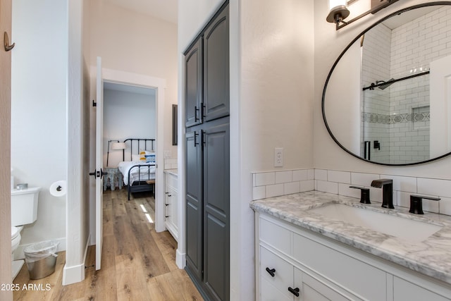 ensuite bathroom with a stall shower, toilet, ensuite bath, wood finished floors, and vanity