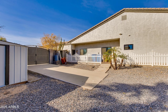 rear view of house with a gate, fence, a patio, and stucco siding