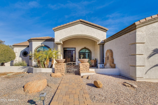 view of exterior entry with a tile roof, a gate, and stucco siding