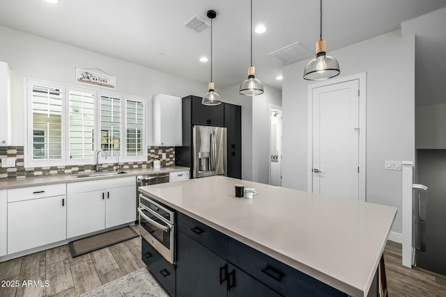 kitchen featuring stainless steel refrigerator with ice dispenser, sink, white cabinetry, a kitchen island, and pendant lighting