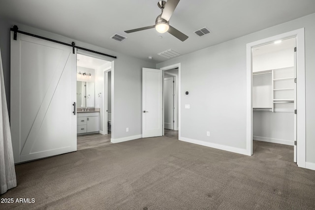 unfurnished bedroom with connected bathroom, carpet floors, a walk in closet, a barn door, and a closet