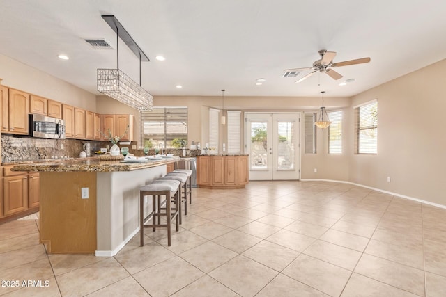 kitchen featuring visible vents, a ceiling fan, stainless steel microwave, backsplash, and a center island