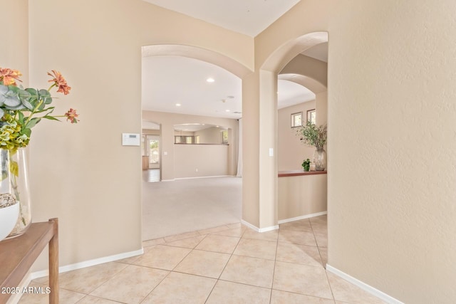 hall featuring light tile patterned floors, a healthy amount of sunlight, arched walkways, and baseboards