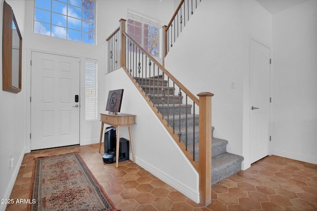 entrance foyer with stairs, baseboards, and a towering ceiling