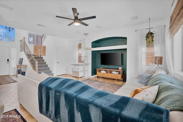 living room with a wealth of natural light, stairway, visible vents, and ceiling fan