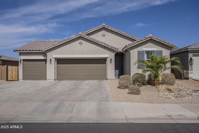 view of front of home featuring decorative driveway, a tile roof, stucco siding, fence, and a garage