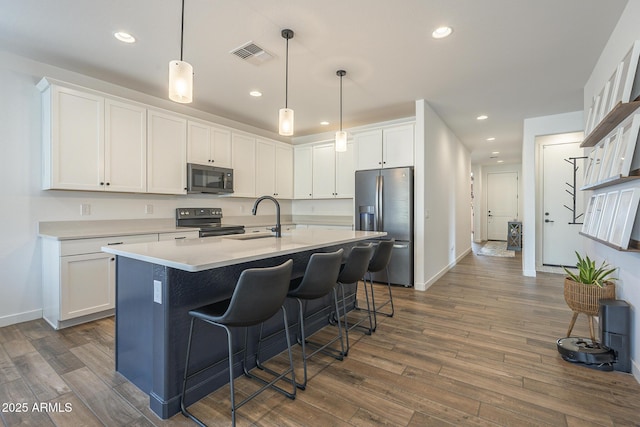 kitchen featuring dark wood finished floors, a breakfast bar area, visible vents, appliances with stainless steel finishes, and a sink