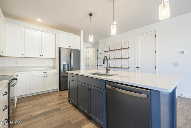 kitchen with wood finished floors, a sink, white cabinets, light countertops, and appliances with stainless steel finishes