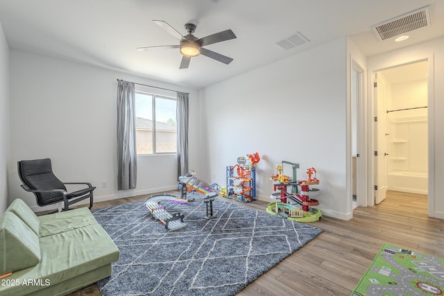 recreation room featuring a ceiling fan, visible vents, baseboards, and wood finished floors