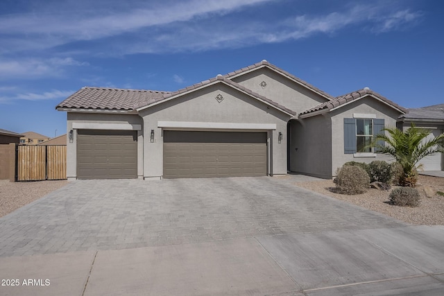 view of front facade with an attached garage, fence, a tiled roof, decorative driveway, and stucco siding