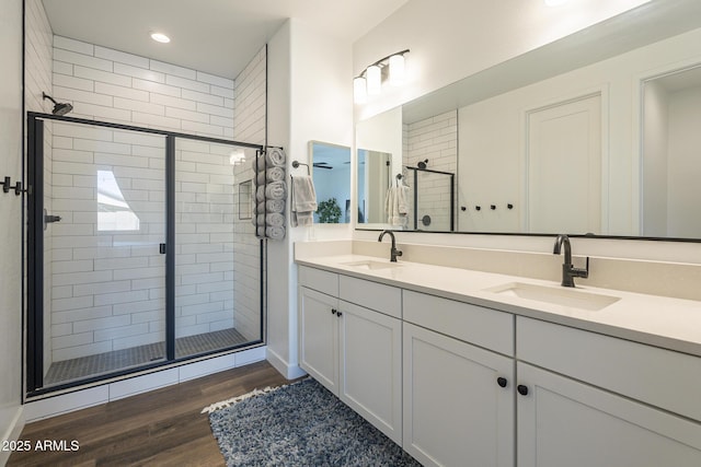 bathroom with double vanity, wood finished floors, a sink, and a shower stall