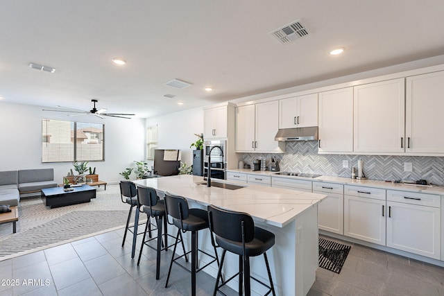 kitchen with an island with sink, under cabinet range hood, visible vents, and white cabinetry