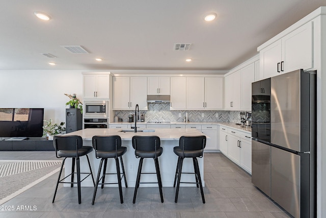 kitchen with stainless steel appliances, visible vents, a center island with sink, and a kitchen bar