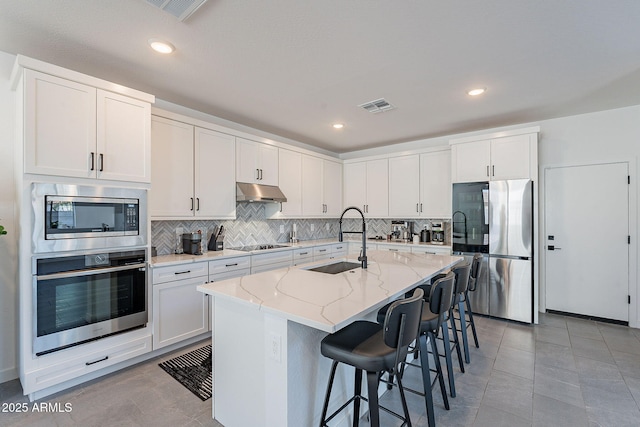 kitchen with visible vents, an island with sink, appliances with stainless steel finishes, under cabinet range hood, and white cabinetry