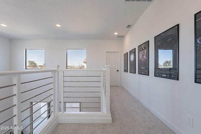 hall with an upstairs landing, light colored carpet, visible vents, and baseboards