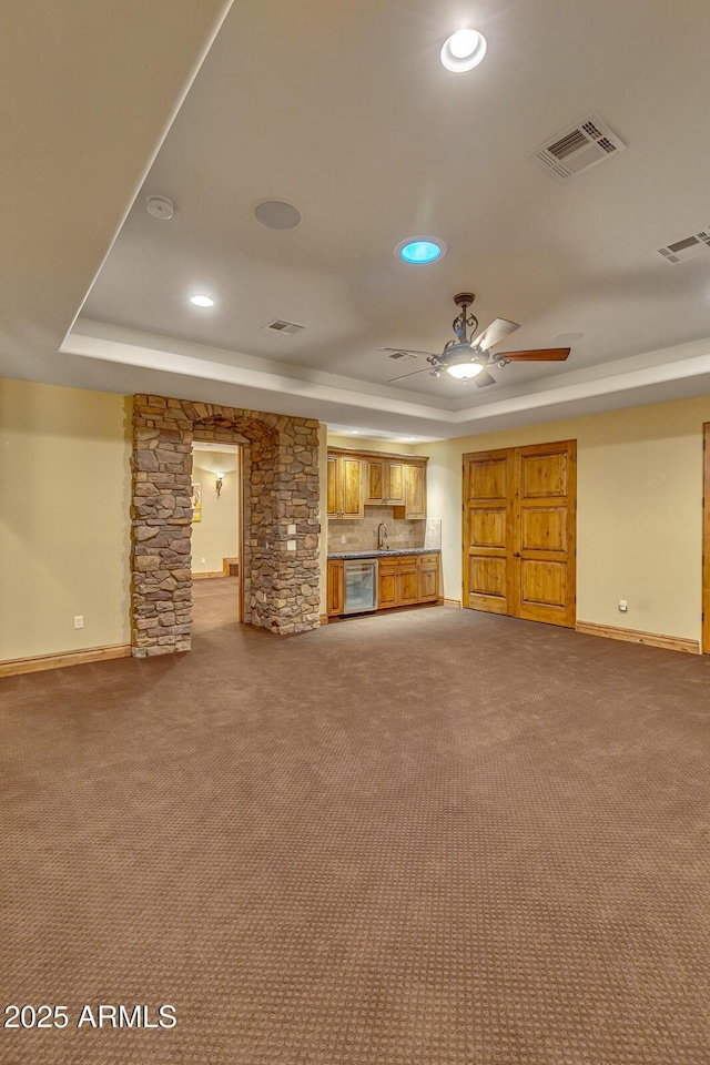 unfurnished living room featuring carpet flooring, a raised ceiling, ceiling fan, and sink