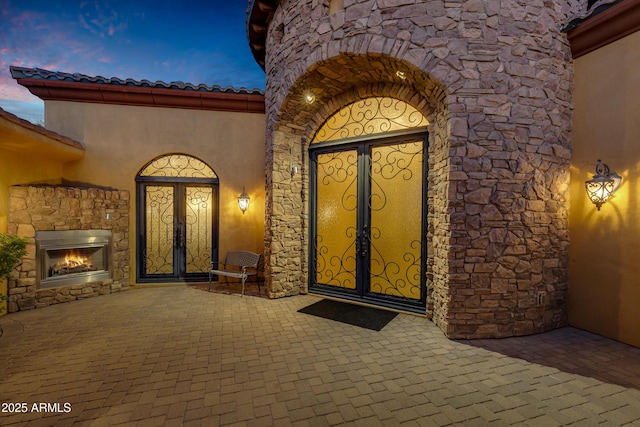 exterior entry at dusk with an outdoor stone fireplace and a patio