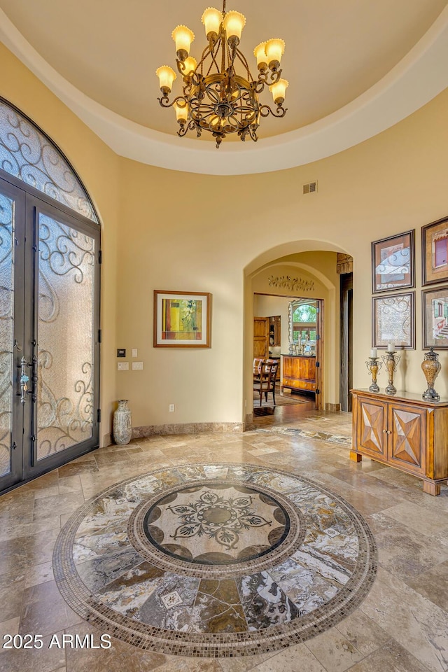 entrance foyer featuring a tray ceiling, french doors, a high ceiling, and a notable chandelier