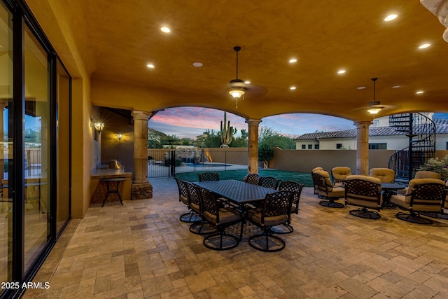 patio terrace at dusk with a fenced in pool and an outdoor kitchen